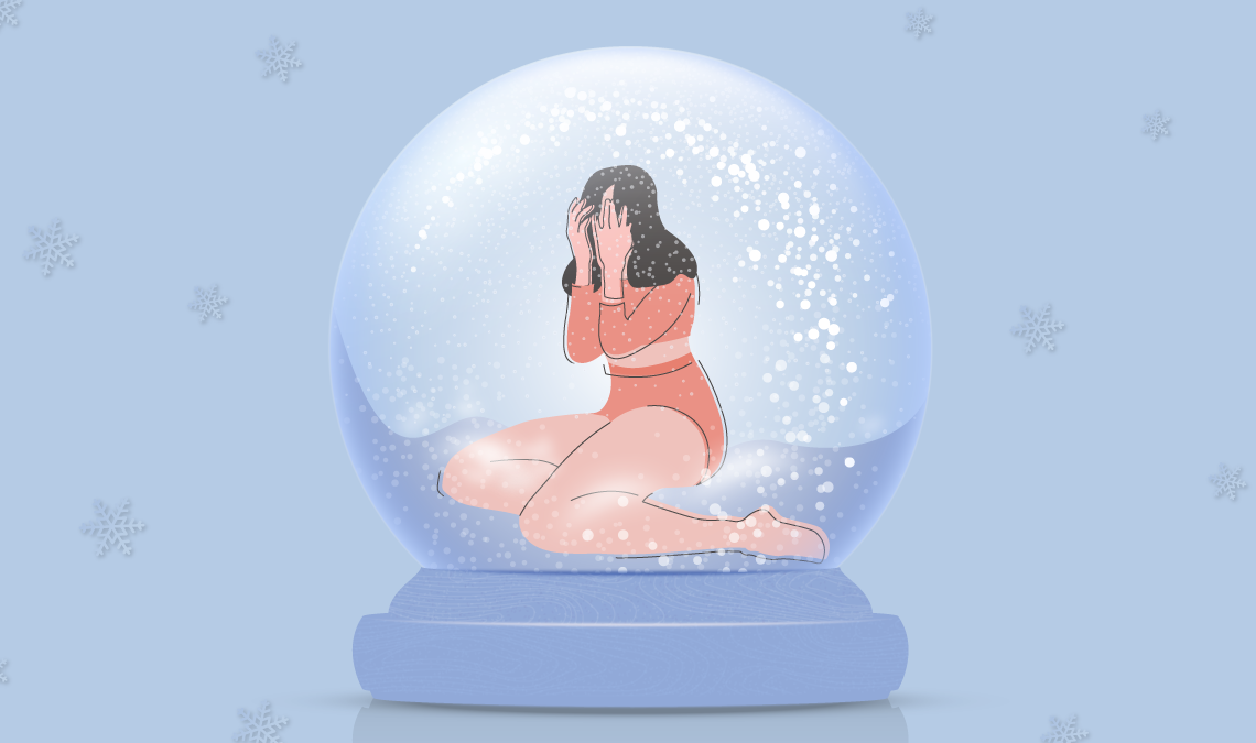 A woman sitting inside a snow globe with her hands on her face, looking sad