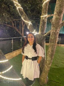 A photograph of Prerna Kalra standing against a lit of tree at nighttime