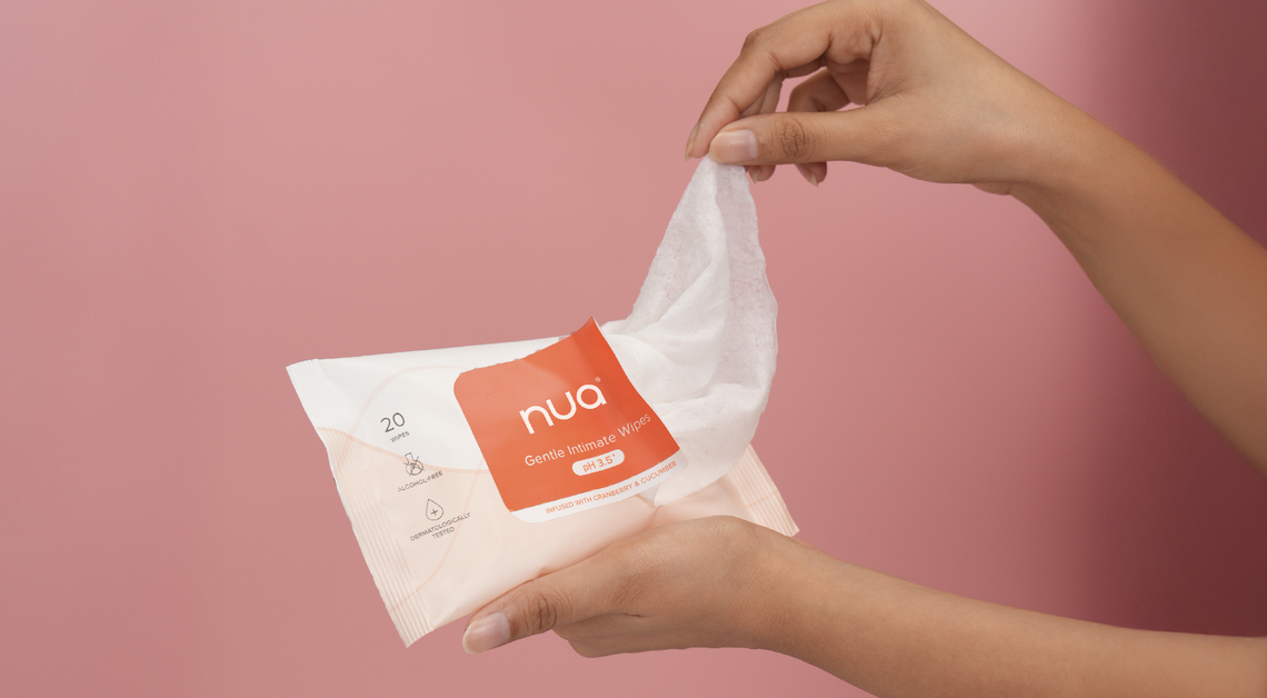 Hands pulling out a Nua Gentle Intimate Wipe from its pack against a pink background.